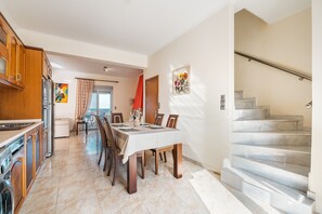 A spacious kitchen with modern appliances, a dining area with a table set for four, and a marble staircase leading to an upper floor.