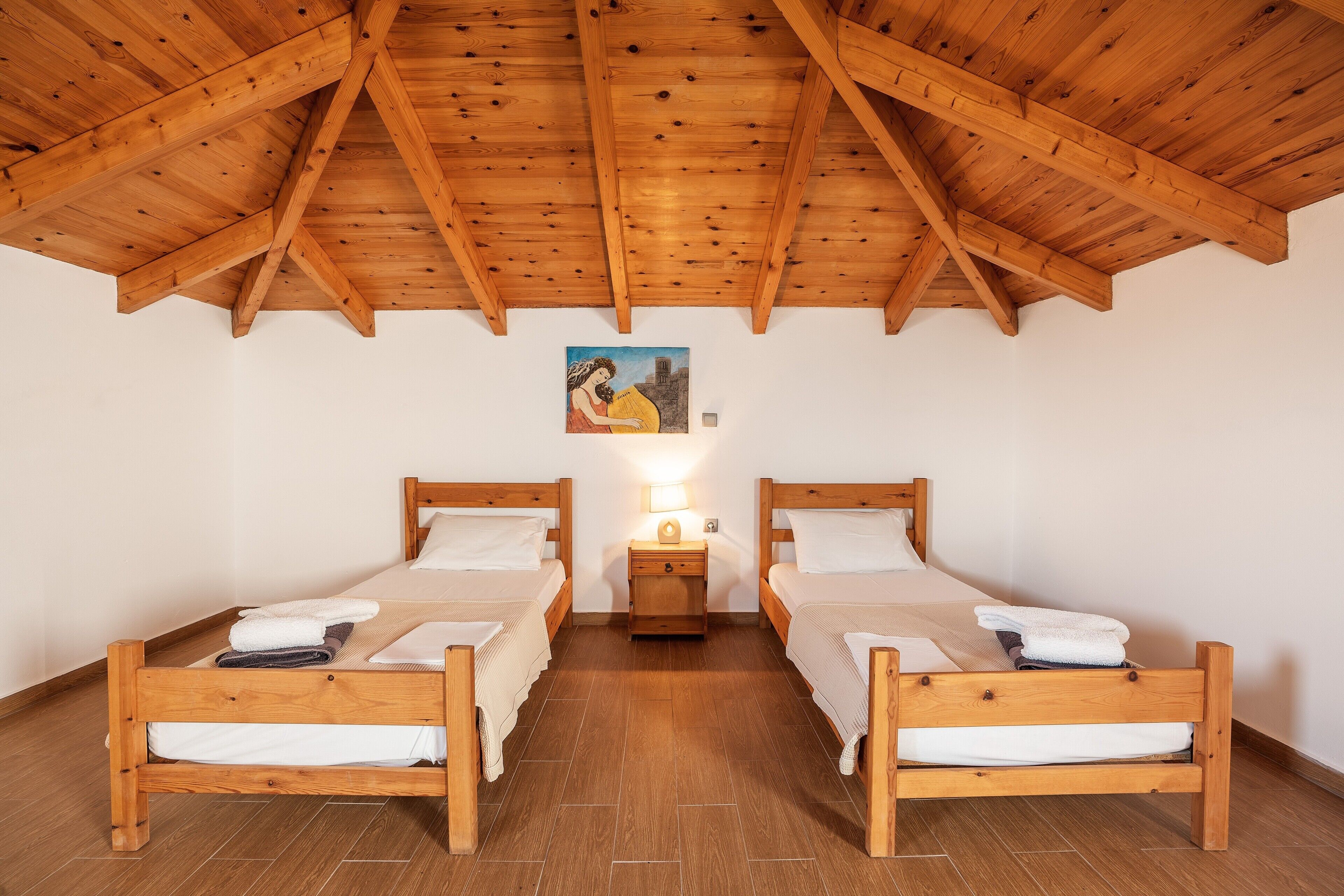 Een kamer met twee houten bedden, een nachtkastje met een lamp en een schilderij aan de muur.