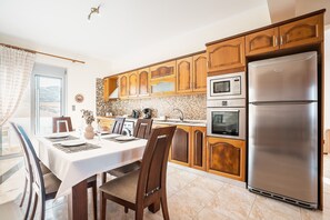 A modern kitchen with wooden cabinets, a stainless steel refrigerator, and a dining area with a table set for four.