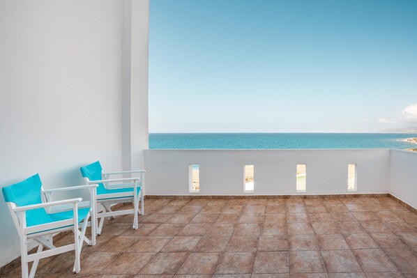 A balcony with two white chairs and a view of the sea.