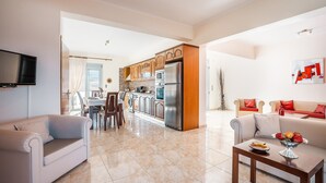 A modern living room with a sofa, a coffee table with fruit, and a kitchen in the background. - Country House 'White Pearl Apolakkia 2' with Shared Pool, Shared Terrace and Wi-Fi (Rhodes)