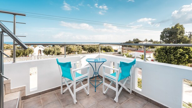 Een balkon met twee witte stoelen en een klein tafeltje, met uitzicht op een heldere lucht en verre gebouwen.