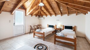 Ein Zimmer mit schrägverlegtem Holzboden, zwei Holzbetten, einem kleinen Tisch, einem Stuhl und einer Tür.