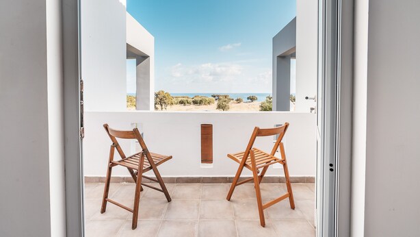 Un balcon avec deux chaises en bois, un mur blanc et une vue dégagée sur la plage.