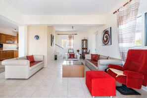 A spacious living area with a sofa, a red armchair, a coffee table, and a kitchen in the background. - Country House 'White Pearl' with Private Pool, Private Terrace and Wi-Fi (Rhodes)
