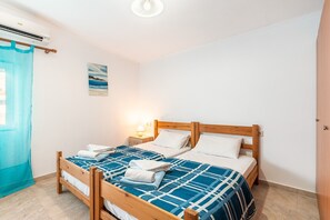 Ein Zimmer mit zwei hölzernen Betten, einem Nachttisch mit Lampe, einem Bild an der Wand und einem Fenster mit Vorhang.