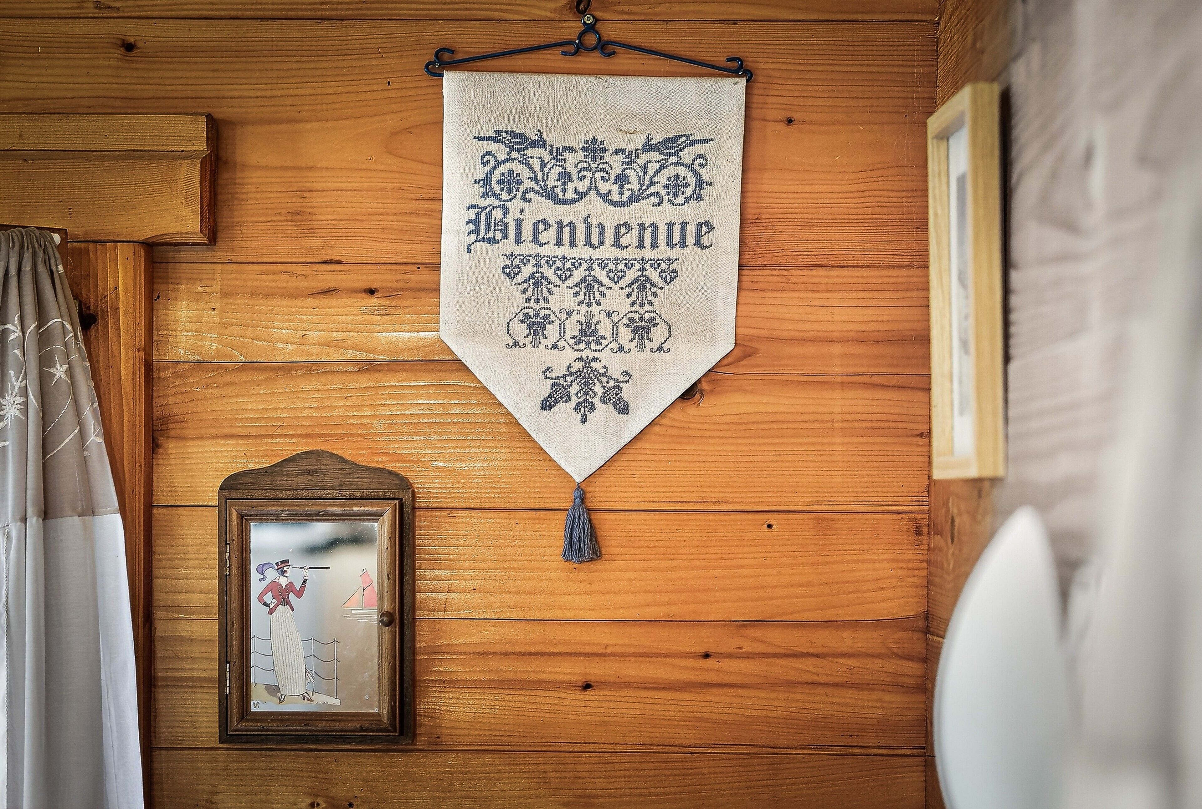 A wooden wall with a hanging welcome banner, a framed picture, and a curtain.