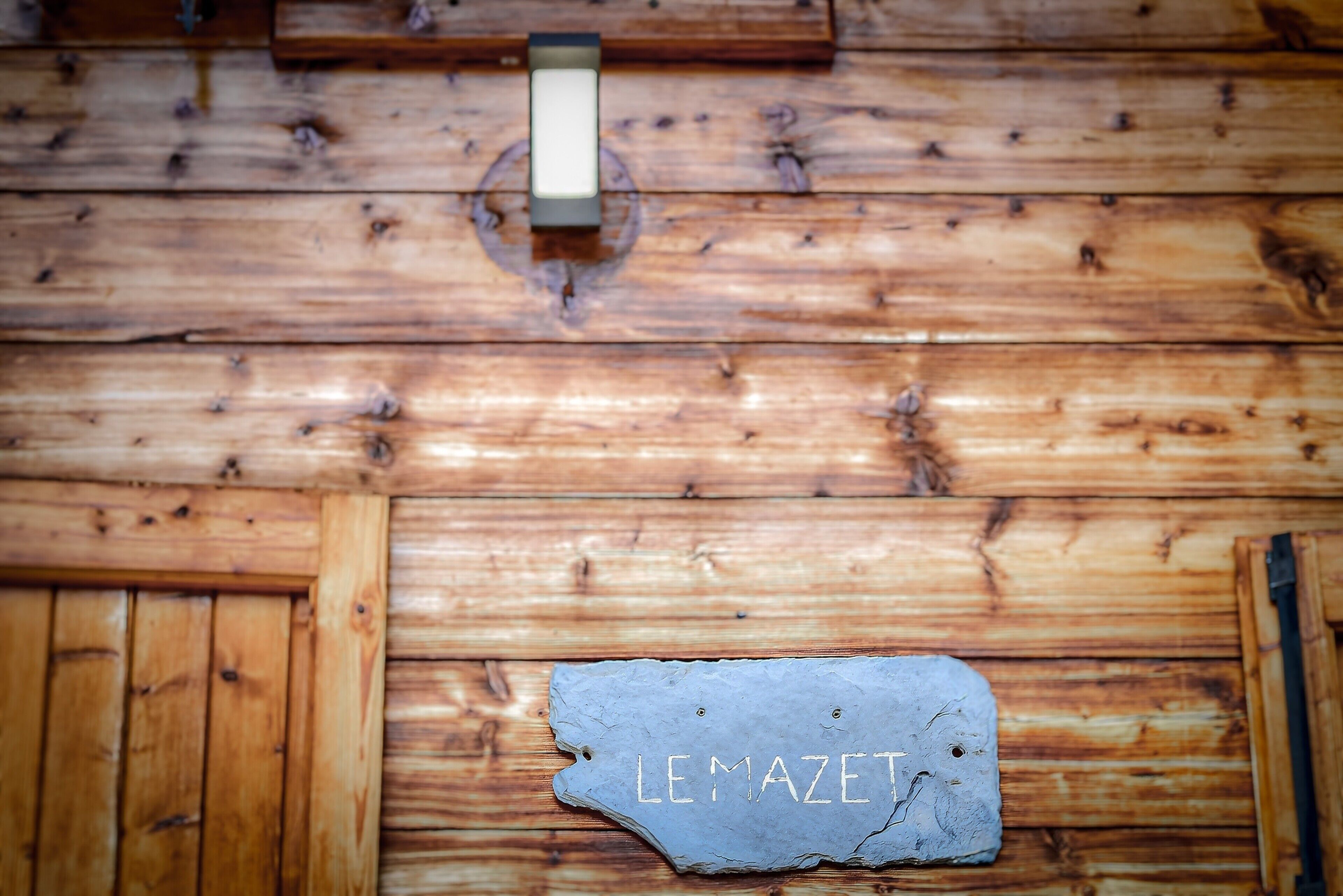 Un mur en bois sur lequel est fixée une plaque d’ardoise portant l’inscription « LE MAZET ».