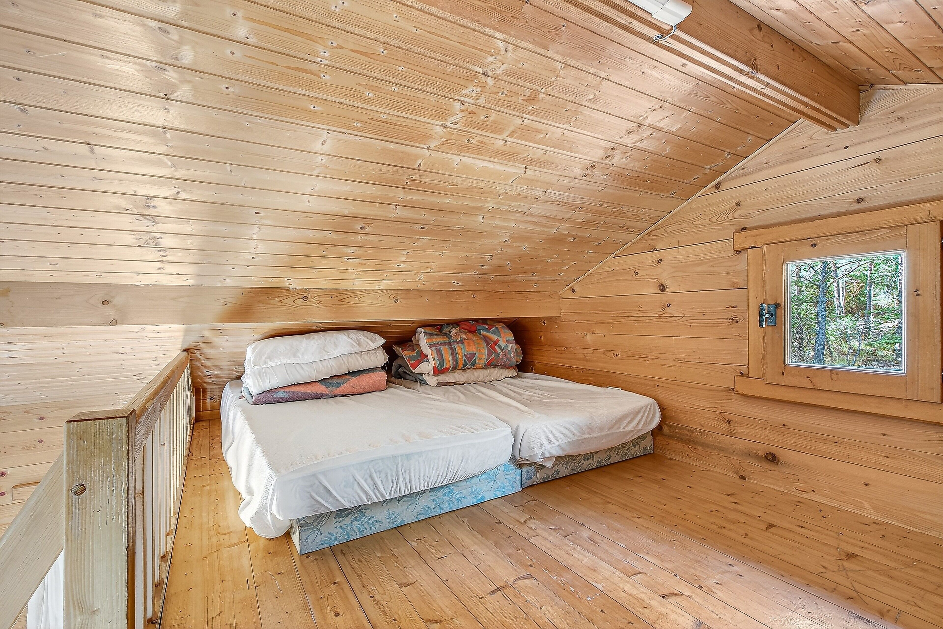 A wooden cabin bedroom with a bed, pillows, and a window.