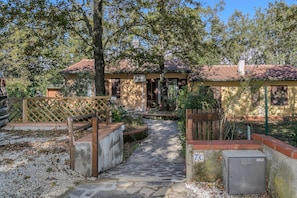 A stone pathway leading to a rustic building with a tiled roof, surrounded by trees and a wooden fence.