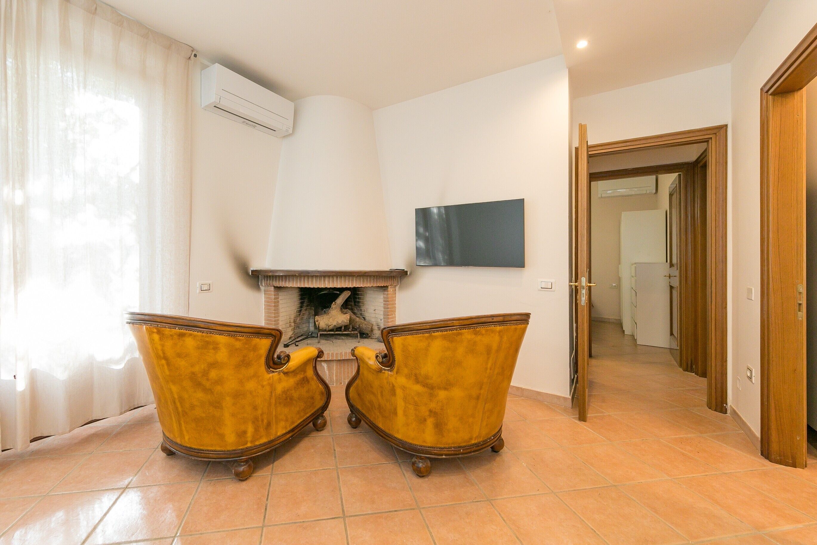 Een kamer met een open haard, twee fauteuils, een flatscreen televisie en een gang naar een andere kamer.