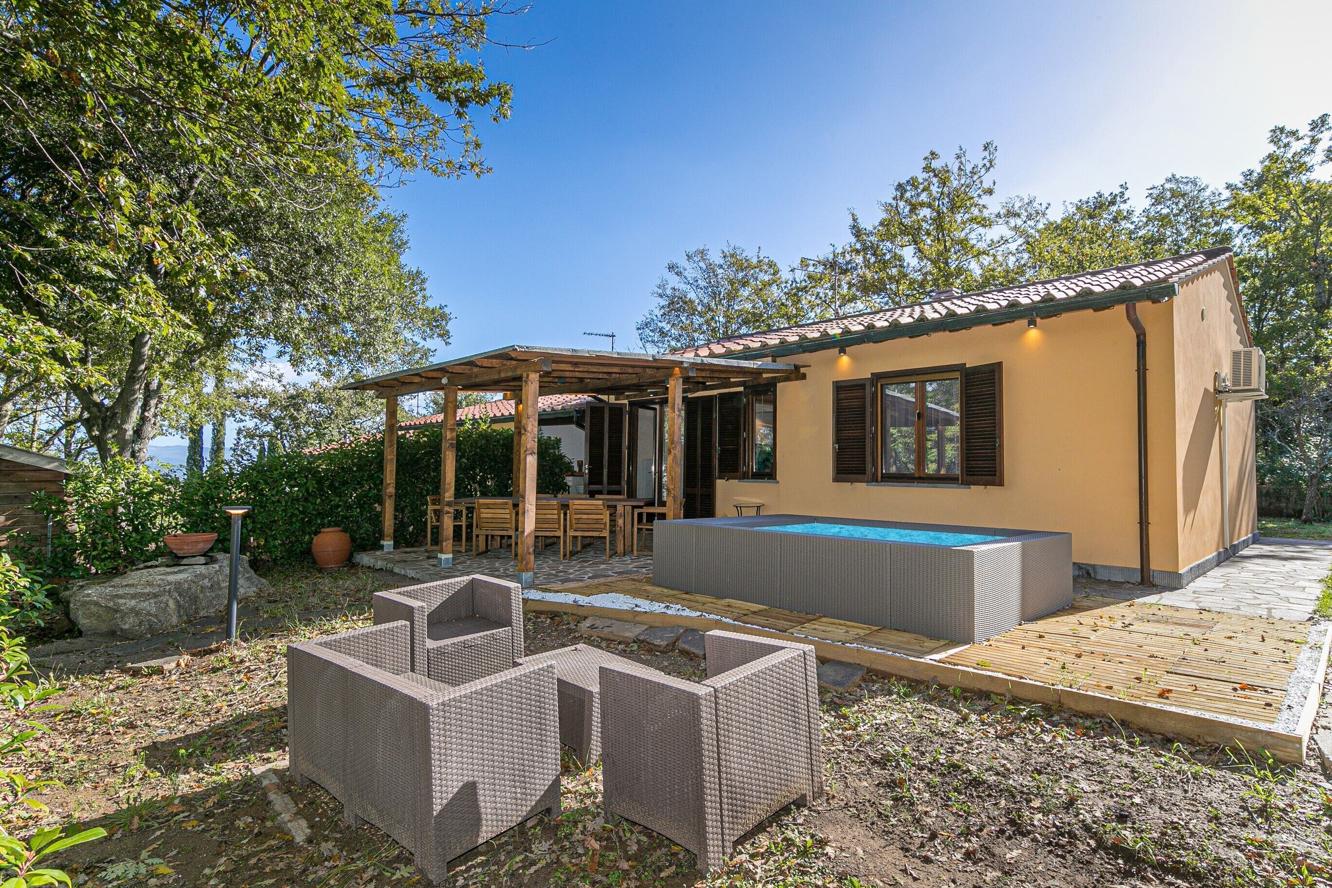 A small house with a pool, outdoor furniture, and a pergola.