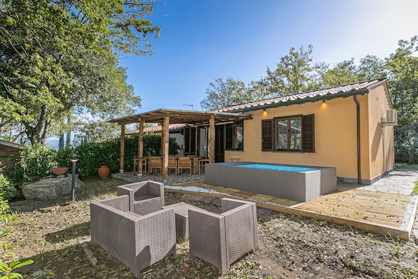 A small house with a pool, outdoor furniture, and a pergola.