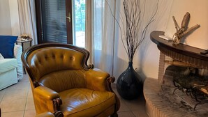 Un salon avec un fauteuil en cuir, un vase décoré de branches et une cheminée.