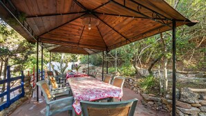 An outdoor covered patio with a table set for dining, surrounded by chairs, and a stone wall. - Vacation Home 'Il Lentischio - Corbezzolo' in Cala Lunga 200 Meters from the Sea (Sant'antioco)