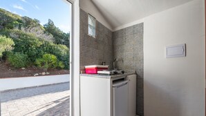 A compact kitchen with a built-in dishwasher, a small countertop, and a window overlooking a landscaped area. - Vacation Home 'Il Lentischio - Corbezzolo' in Cala Lunga 200 Meters from the Sea (Sant'antioco)