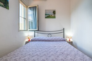 Une chambre à coucher avec un lit, une fenêtre avec des rideaux, une table de chevet avec une lampe et un tableau accroché au mur.