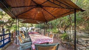 An outdoor covered patio with a long dining table, chairs, and a stone wall backdrop. - Vacation Home 'Il Lentischio - Rosmarino' in Cala Lunga 200 Metres from the Sea (Sant'antioco)