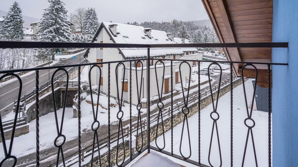 Varanda com grades de metal com vista para uma área residencial coberta de neve, com casas e árvores.