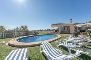A swimming pool with lounge chairs, a covered patio, and a fenced garden.