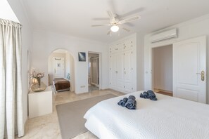 A bedroom with a bed, a ceiling fan, a bathroom visible through an archway, and a wardrobe.