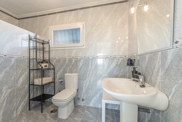 A bathroom with a toilet, a sink, a mirror, and a shelf with toiletries. - Villa 'Villa in Mijas Golf' with Sea View, Wi-Fi and Air Conditioning (Mijas)