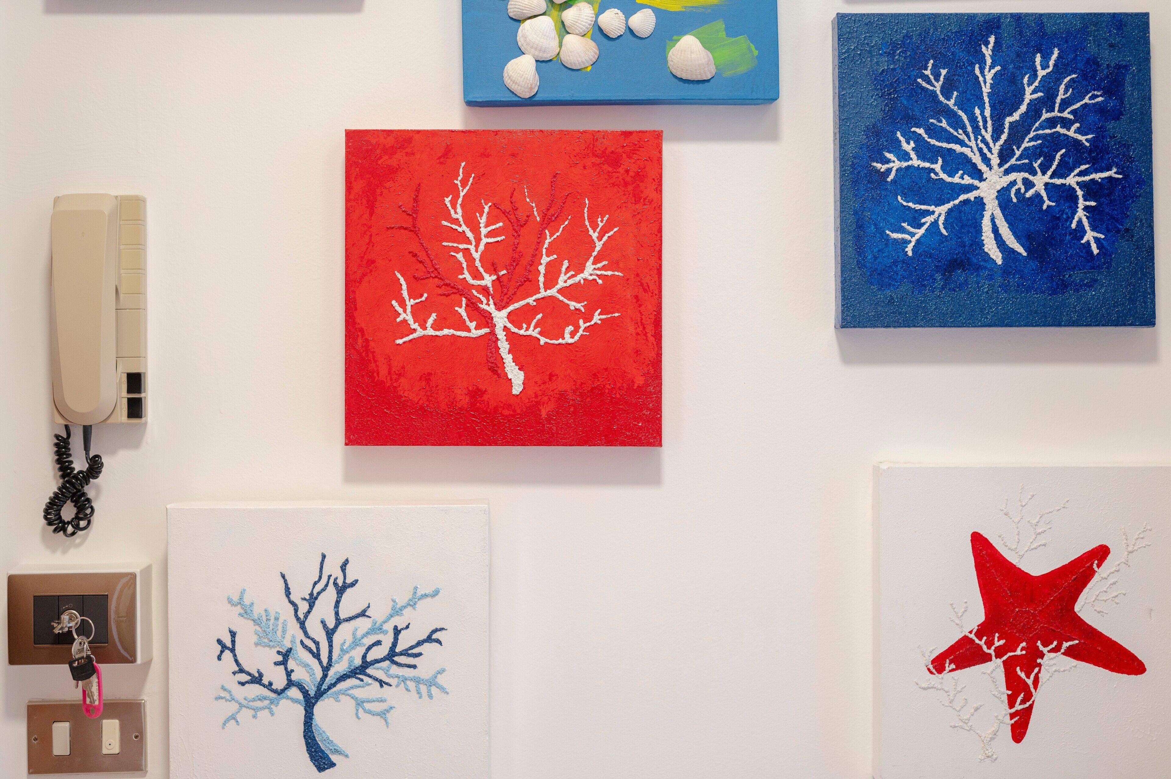 A wall with various artworks, a phone, and a wall socket.