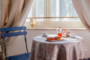 Une table de petit-déjeuner avec un pichet, des tasses et des viennoiseries, placée devant une fenêtre ornée de rideaux.