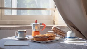 Une table près d’une fenêtre est dressée pour le petit-déjeuner, avec une cafetière, des tasses et des viennoiseries.