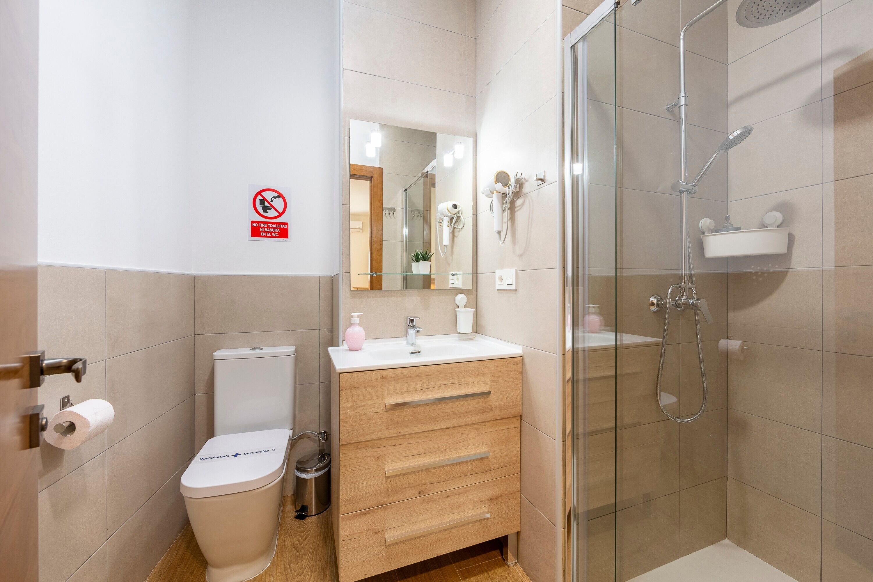A bathroom with a toilet, sink, mirror, and shower.