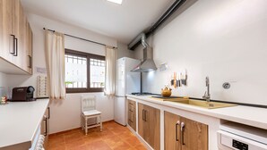 Une cuisine moderne avec un plan de travail blanc, des armoires en bois, un four encastré et une fenêtre avec des rideaux.