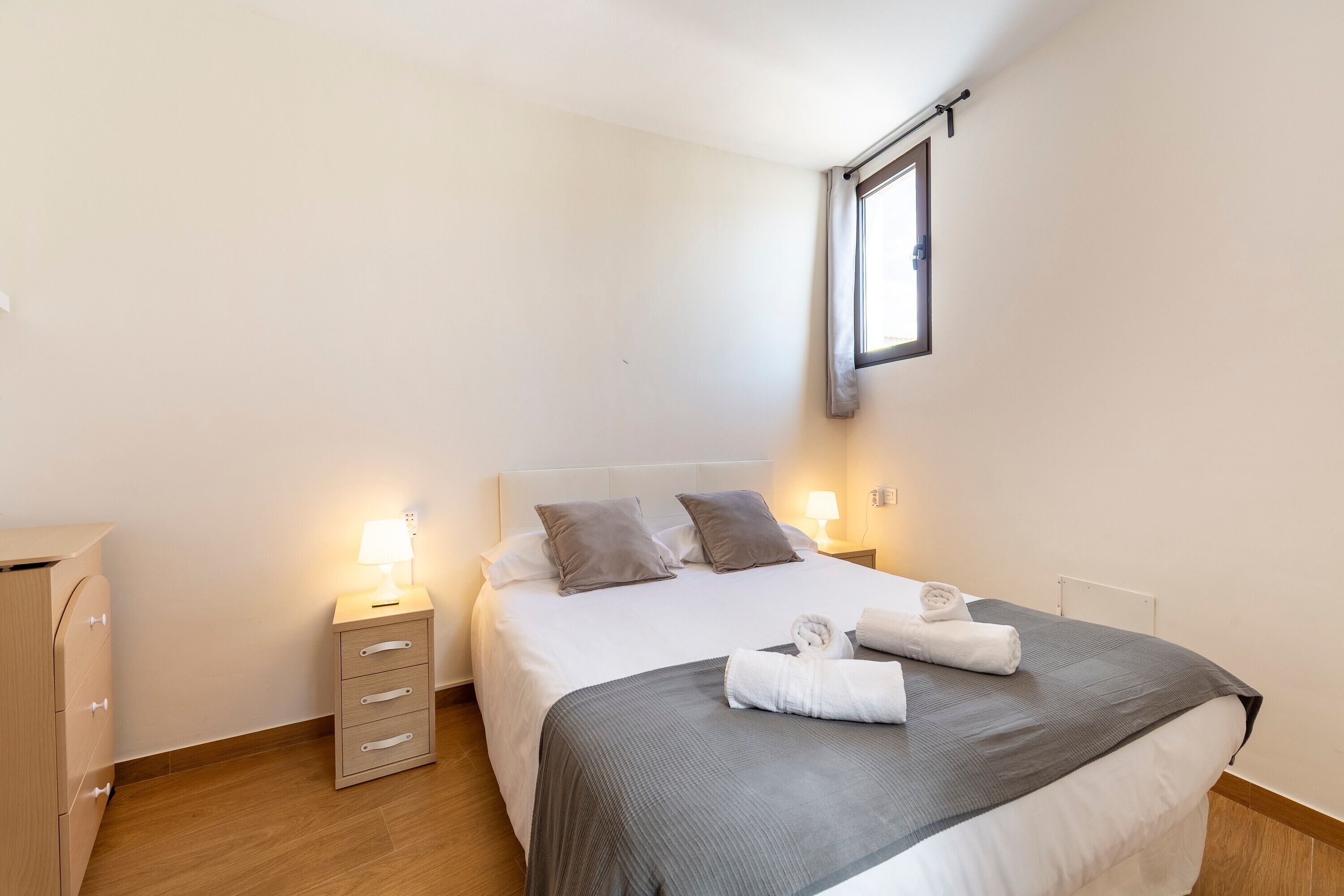 Un dormitorio ordenado con cama, mesitas de noche, un armario y una ventana.