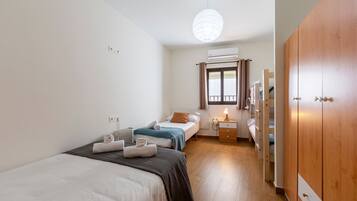 Een slaapkamer met twee bedden, een houten garderobe, een nachtkastje met een lamp en een airconditioning.