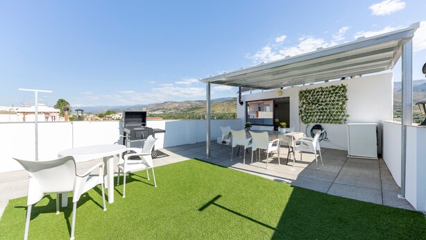Une terrasse sur le toit avec une table et des chaises blanches, un barbecue et un mur recouvert d’un jardin vertical.