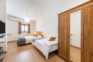 A bedroom with two beds, a wardrobe, a television, and a window with curtains. - La Casa de la Buhardilla – Rural House with Sierra Nevada Views in Fondón (Fondón)
