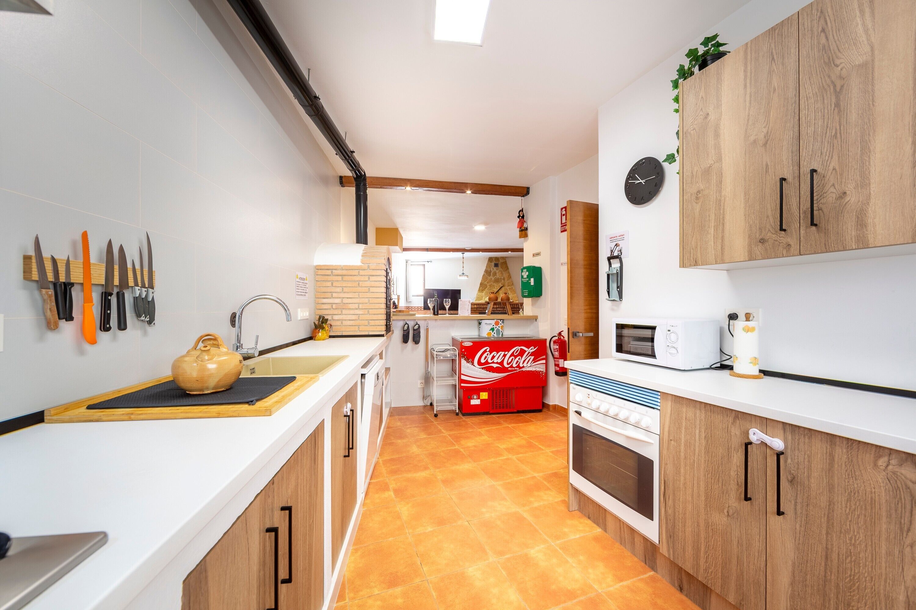 Una cocina moderna con encimeras blancas, armarios de madera, un microondas y un refrigerador rojo Coca-Cola.