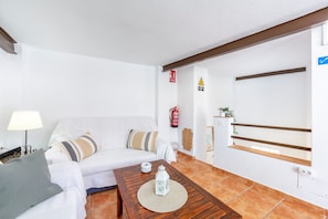 A living room with a white sofa, a wooden coffee table, a lamp, and a fire extinguisher on the wall. - La Casa de la Buhardilla – Rural House with Sierra Nevada Views in Fondón (Fondón)