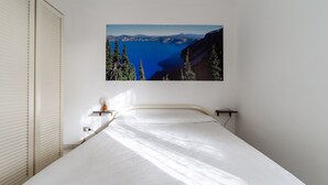 Ein Schlafzimmer mit einem Bett, einem an der Wand hängenden Landschaftsbild und einem Nachttisch mit einer Lampe.