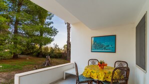 Eine Terrasse mit Tisch und Stühlen, ein Bild an der Wand und Blick auf Bäume.