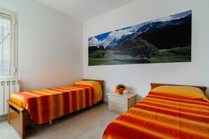 Une chambre avec deux lits, une table de chevet, une fenêtre et un tableau représentant un paysage de montagne accroché au mur.
