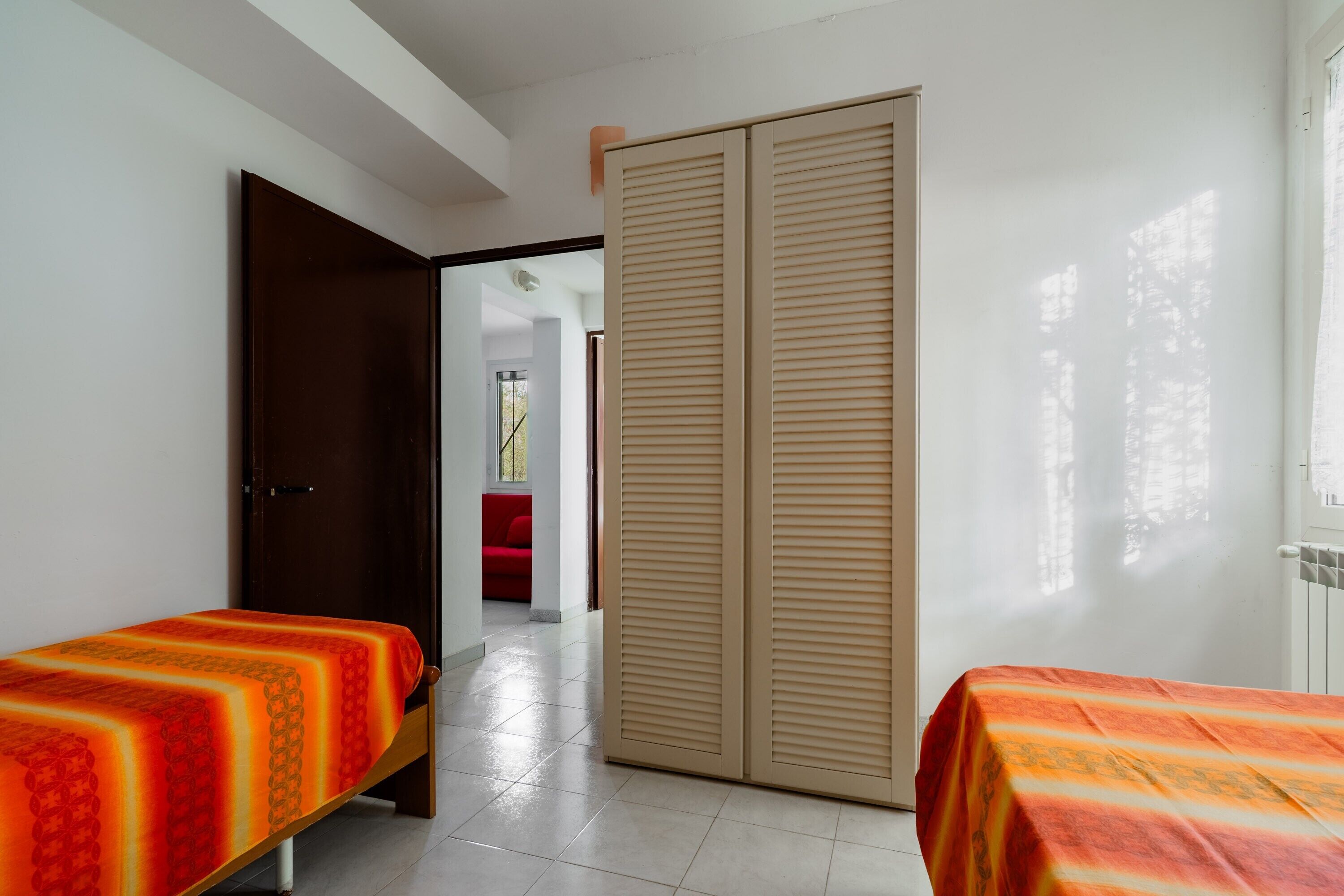 A hotel room with two beds, a large sliding door, and a view of a red chair through an open door.