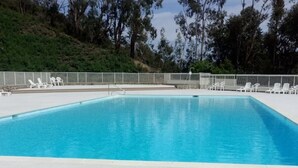 A clear blue swimming pool with white lounge chairs and a white deck.