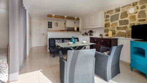 A modern kitchen with a stone wall, a dining area with wicker furniture, and a TV on a wooden cabinet.