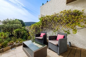 An outdoor patio with wicker furniture, a glass table, and a white wall with climbing plants.