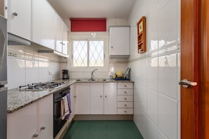 A compact kitchen with white cabinets, a gas stove, a sink, and a window.