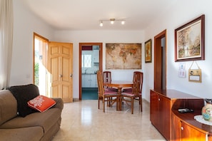 A living room with a sofa, a dining table with chairs, a wooden cabinet, and a painting on the wall.