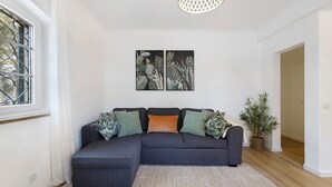 A living room with a sectional sofa, a patterned rug, a potted plant, and a wall-mounted artwork. - Apartment 'Jardim Da Parada' with Wi-Fi and Air Conditioning (Cascais)