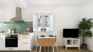 A compact kitchen with a built-in oven, a window with decorative ironwork, a dining table with chairs, and a television on a stand. - Apartment 'Jardim Da Parada' with Wi-Fi and Air Conditioning (Cascais)
