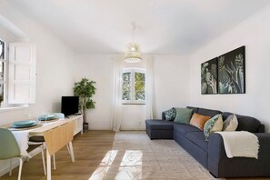 A living room with a sofa, a dining table, a TV, and a window with curtains.