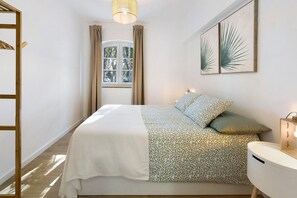 A bedroom with a bed, a bedside table, a window with curtains, and wall art.